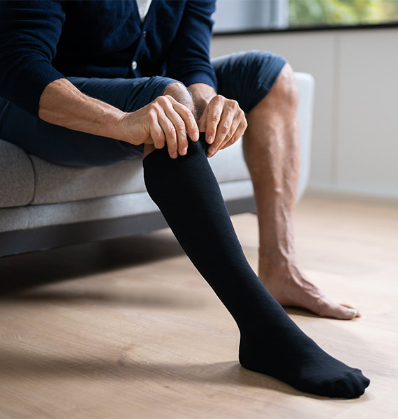 Man sitting on the edge of his bed putting on compression socks.